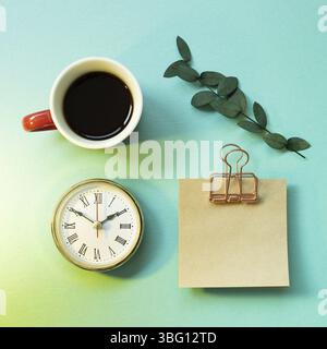 Notepad, clock, cup of coffee, green leaf on mint green background. office desk, workspace. top view Stock Photo