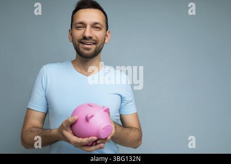 Photo of happy cute smiling young handsome brunet unshaven man with beard with sincere emotions wearing casual blue t-shirt isolated over blue backgro Stock Photo