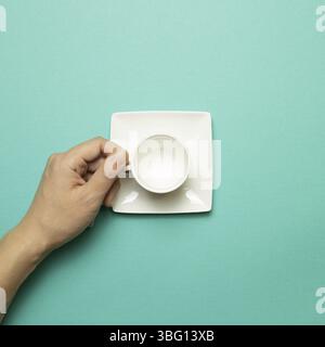 Female hand holding white empty mug cup on mint green background. top view Stock Photo