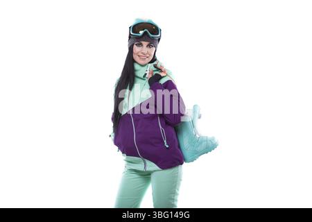 Isolated on white, attractive caucasian woman in purple ski outfit, blue ski glasses and blue trousers hold blue snow boots Stock Photo