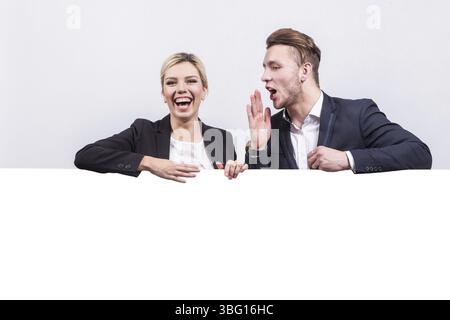 Couple of young caucasian businesswoman with ponytail in black suit and businessman in black suit relies on empty bottom part Isolated on grey Stock Photo