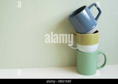 Stack of blue and green mug cups on white table. mint wall background. copy space Stock Photo