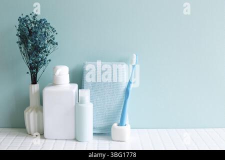Bathroom bottles, shower towel, toothbrush, vase of plant on white mosaic tile table. blue wall background. Skin care and spa concept. Home interior Stock Photo