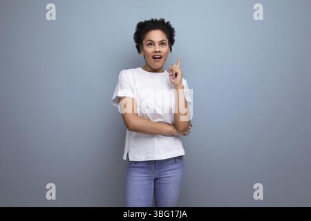 A young brunette woman with afro hair in a white t-shirt demonstrates with inspiration with the help of her hands an advertisement Stock Photo