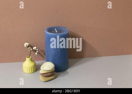 Navy candle and stack of pebble stones and dry plant on gray table. brown wall background. home decor interior Stock Photo