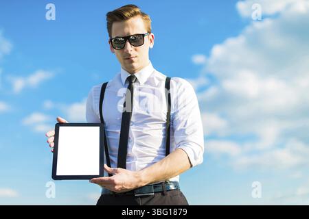Serious attractive brunette caucasian businessman in white shirt, black tie, black braces, costly watch and black sunglasses stand on the green ladder Stock Photo