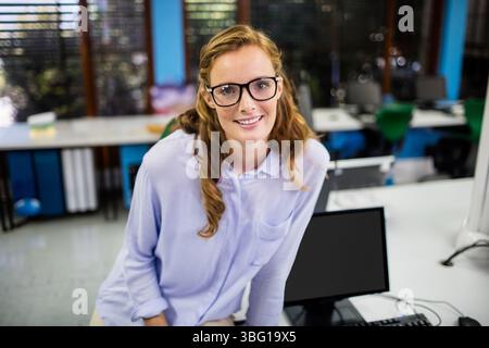 Office worker wearing eyeglasses leaning on desk typing on keyboard near computer monitor in office Stock Photo