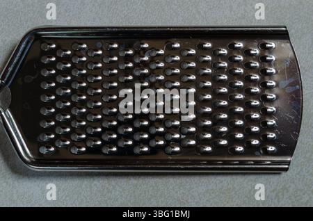 Hand held steel cheese grater on a gray patterned background Stock Photo