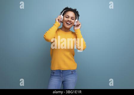 Cheerful young hispanic business woman with black curly hair listening to music in white headphones Stock Photo