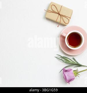 Gift box and cup of black tea with pink rose flower on white background. Flat lay, top view, copy space Stock Photo