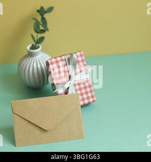 Gift box, plant, envelope on green table. yellow wall background Stock Photo