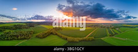 High resolution wide angle drone panorama aerial view of summer sunset over green field patches and cluster of trees, sun setting down and nice clouds Stock Photo