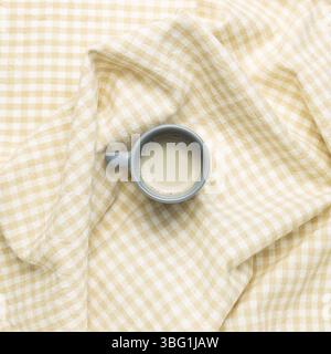 Cup of milk tea on crumpled beige check pattern fabric background. top view Stock Photo