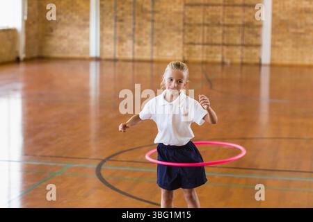 Girl spinning bright pink hula hoop in school gymnasium with colored court lines on hardwood floor Stock Photo