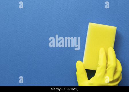 Hand in yellow glove hold sponge on blue background. Cleaning concept. top view, copy space Stock Photo