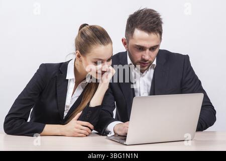 Man and woman sitting in a business suit at a table in front of a laptop and looking at its screen Stock Photo