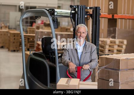 Red-handled pallet jack is waiting on concrete floor among stacked cardboard boxes inside warehouse Stock Photo