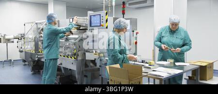 Pharmaceutical technicians work in sterile working conditions at pharmaceutical factory. Scientists wearing protective clothing Stock Photo