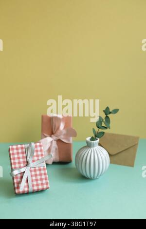 Gift box, plant, envelope on green table. yellow wall background Stock Photo