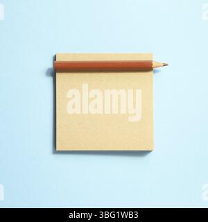 Memo note pad and brown colored pencil on blue background Stock Photo