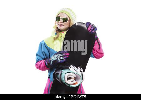 Isolated on white, blonde attractive caucasian girl in colorful ski suit and purple ski gloves hold black snowboard Stock Photo