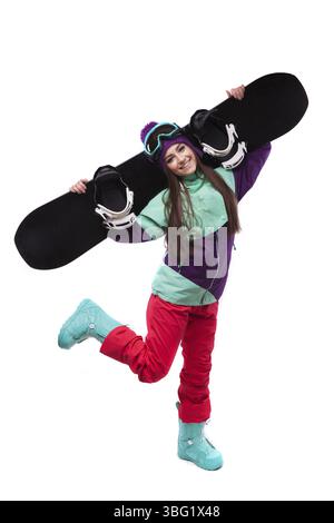 Isolated on white, brunette pretty young caucasian woman in purple ski outfit, blue snow boots and blue ski goggles stand on one leg and hold black sn Stock Photo