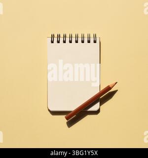 Blank notebook and colored pencil on beige background. top view, copy space Stock Photo