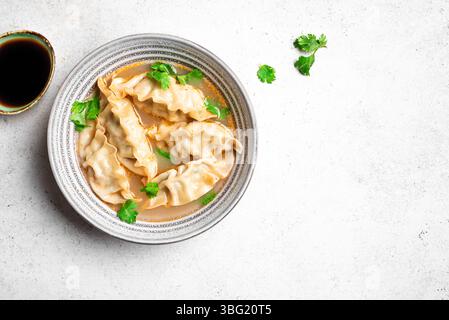 Wonton soup bowl on white concrete background, top view, copy space. Shrimp or pork wonton soup with ciliantro, top view. Asian style lunch - dumpling Stock Photo