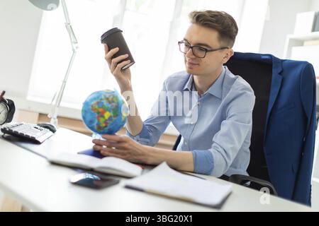 A handsome young man with glasses, blue trousers and a light shirt is working in the office. On the back of the chair hangs his jacket. photo with dep Stock Photo