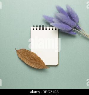 Empty notebook with tail grass, dry leaf on green background. top view, copy space Stock Photo