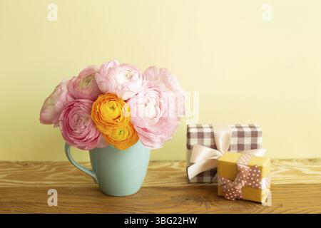 Gift boxes and vase of ranunculus flowers on wooden table. yellow background Stock Photo