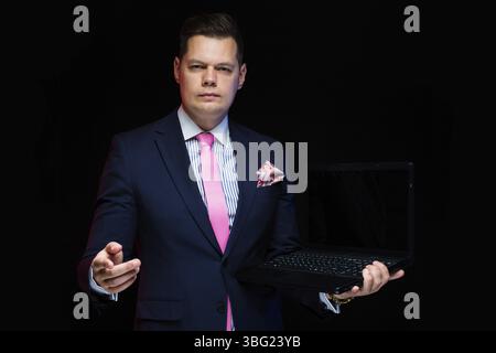 Young caucasian elegant smart clever friendly business man serious thoughtful in blue suit standing in office looking in camera with laptop Stock Photo