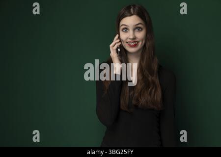A woman is actively engaged in a conversation on her cell phone, holding the device up to her ear with a focused expression. She appears to be standin Stock Photo