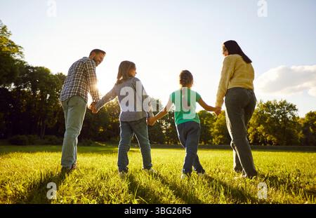 Back view of father, mother, daughter son holding hands together standing in fiend on green grass Stock Photo