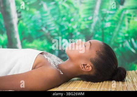 Woman lying face-up on bamboo mat wrapped in white towel, showing scrub crystals in tropical spa Stock Photo
