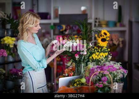 Female florist misting daisies and pink carnations with pink spray bottle at worktable Stock Photo