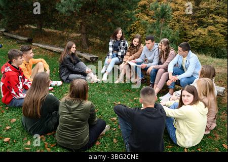 Ivano-Frankivsk, Ukraine September 22, 2023:A group of teenagers are sitting in a circle on a grassy area, engaged in a lively discussion. Autumn leav Stock Photo