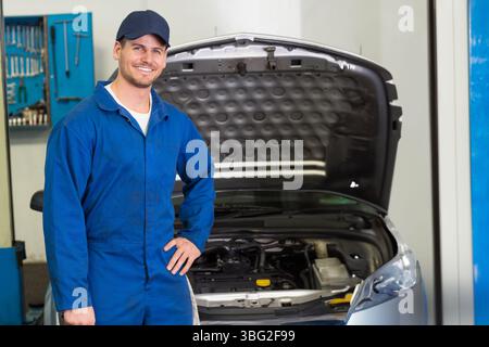 Male mechanic standing beside silver car with open hood at garage showing engine, tools, copy space Stock Photo