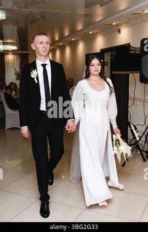 Ivano-Frankivsk, Ukraine September 28, 2024:A newly married couple walks into their reception, the bride in a stunning white gown, the groom in a clas Stock Photo
