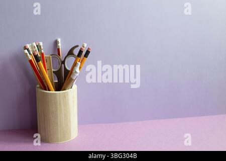 Pencils and various stationery in wooden holder on purple desk. purple wall background Stock Photo