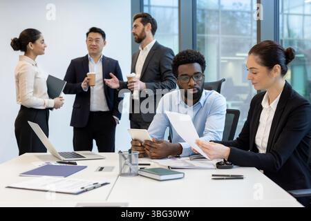 Diverse business team collaborating in a modern office setting, focusing on documents and technology for their project. Stock Photo