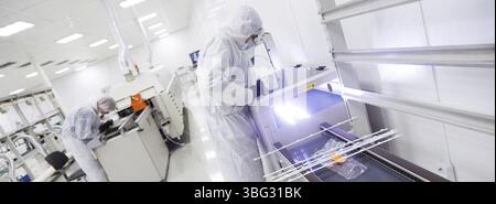 Factory workers in white lab suits and black latex gloves, working with some modern equipment in a very clean room Stock Photo