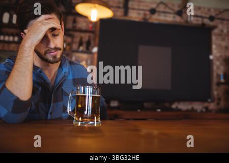 Glass mug of beer resting on bar counter beneath glowing pendant lamp against exposed brick wall Stock Photo