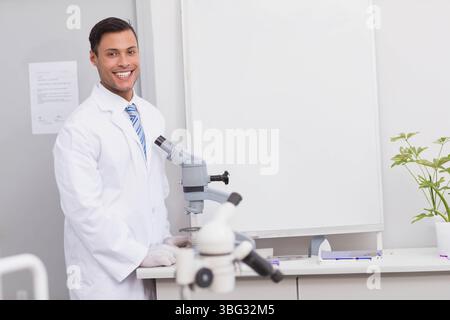 Male researcher standing at lab bench wearing lab coat, gloves operating microscopes, copy space Stock Photo