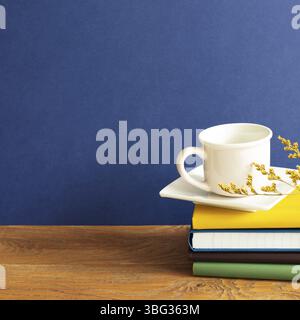 Stack of notebooks and coffee cup on wooden desk. blue wall background Stock Photo
