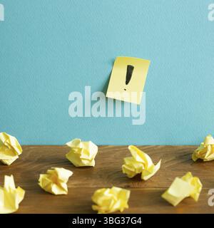 Crumpled paper balls and notepad with exclamation mark on wooden desk. blue wall background. Thinking, solution, business, idea concept Stock Photo