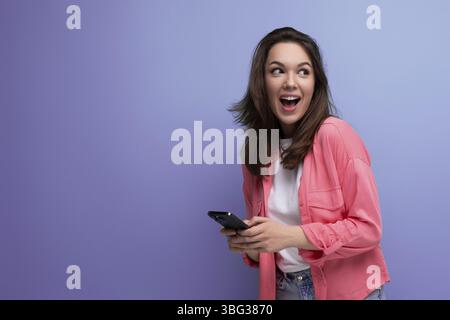 Brunette young woman with shoulder-length hair in a pink shirt with a smartphone isolated on a plain background Stock Photo
