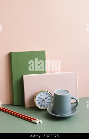 Notebook, clock, coffee cup, pencil on green desk. pink wall background. workspace Stock Photo