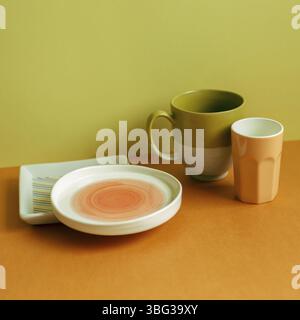 Empty plate and mug cup on orange table. yellow green wall background Stock Photo