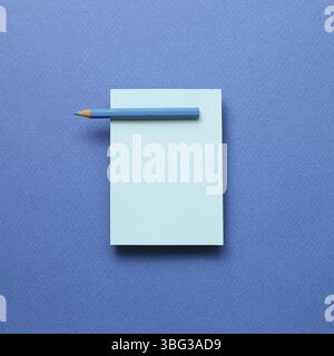 Blue memo note pad and blue colored pencil on blue background Stock Photo